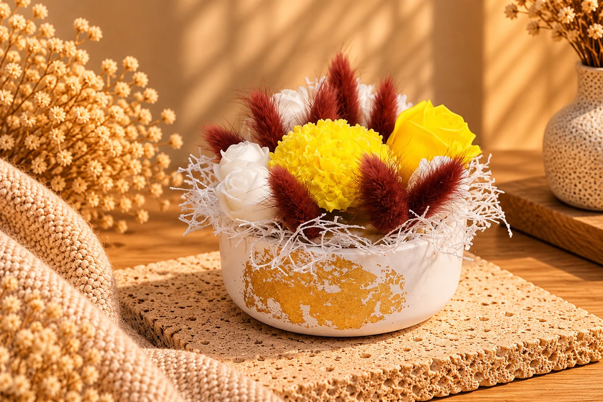 Amalfi Bouquet Wax Haven με έντονα κίτρινα και λευκά λουλούδια από κερί, μπορντό διακοσμητικά στάχυα και λευκά κλαδάκια σε λευκό δοχείο με χρυσές λεπτομέρειες